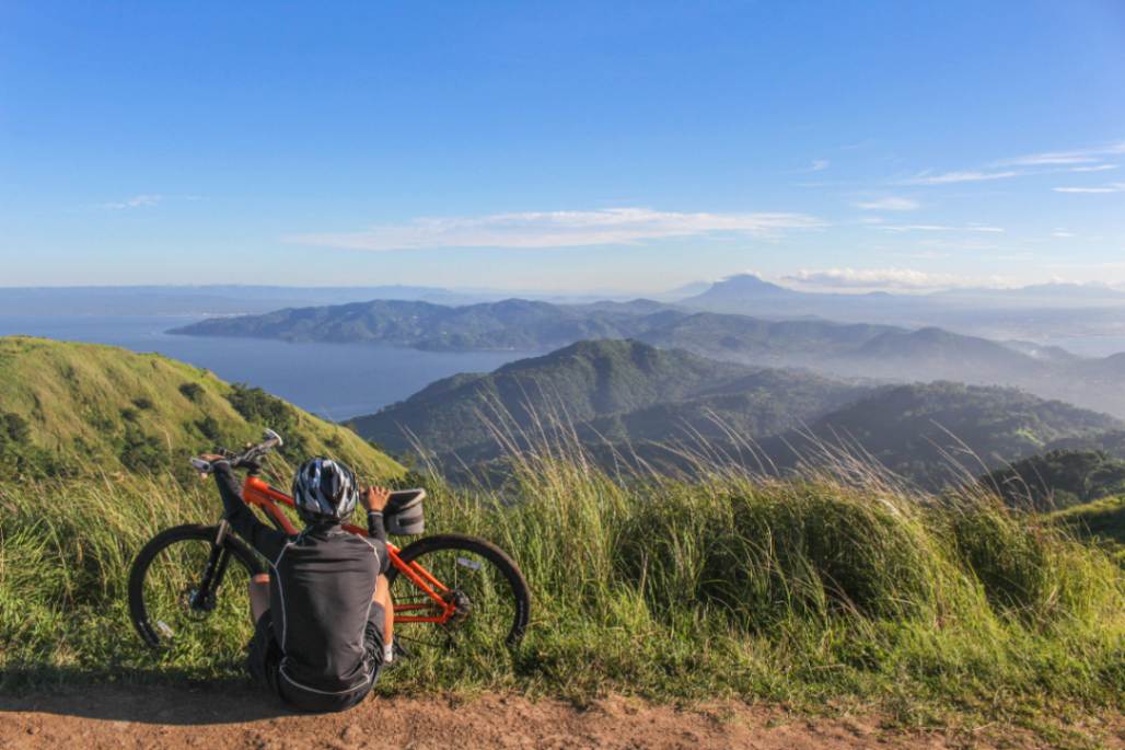 Mountain biker sat down holding orange eMTB and looking at mountains and the sea beyond